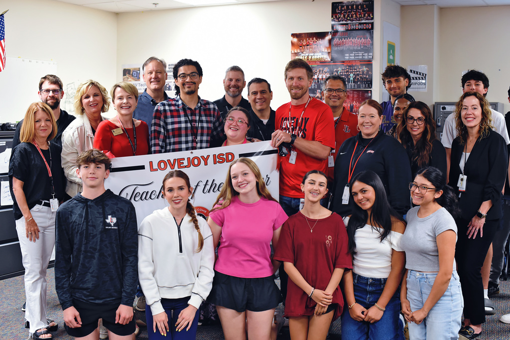 A diverse group of individuals in a classroom posing with a banner that reads "LOVEJOY ISD Teacher of the Year".