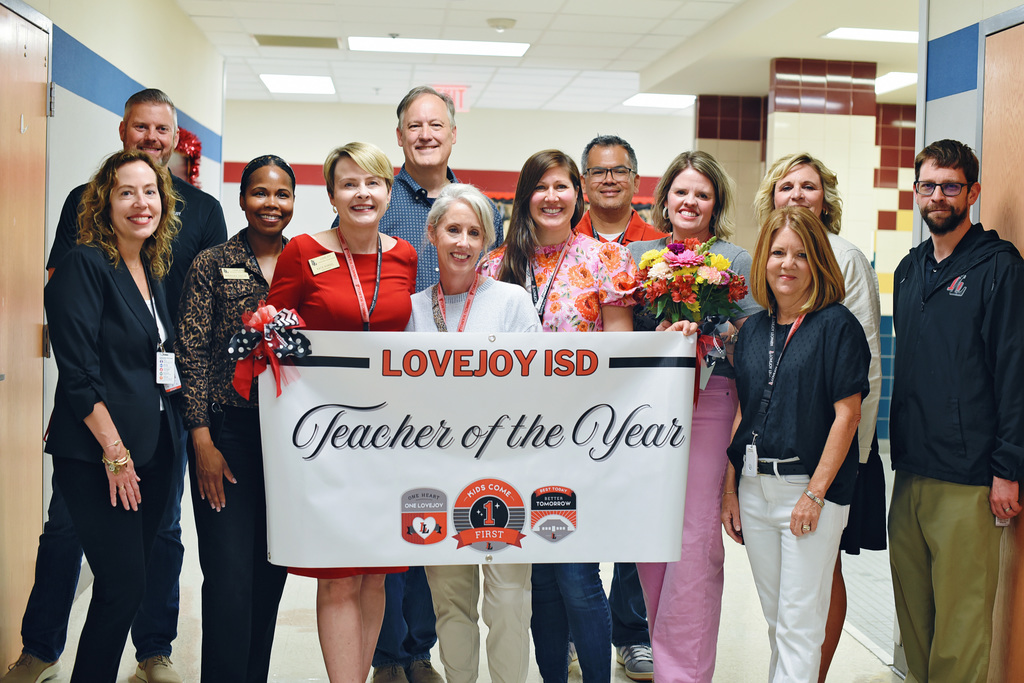 Group of people in a hallway. One woman holds a banner that says "Teacher of the Year."