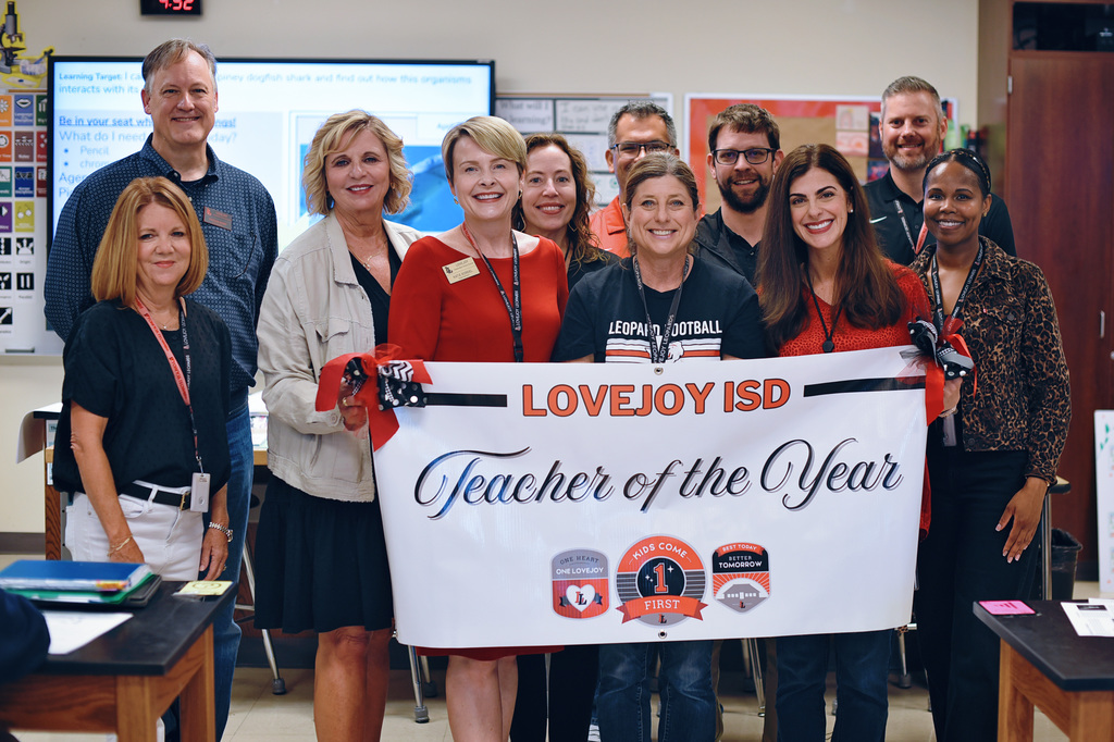A group of people posing for a photo holding a banner that reads "Teacher of the Year".