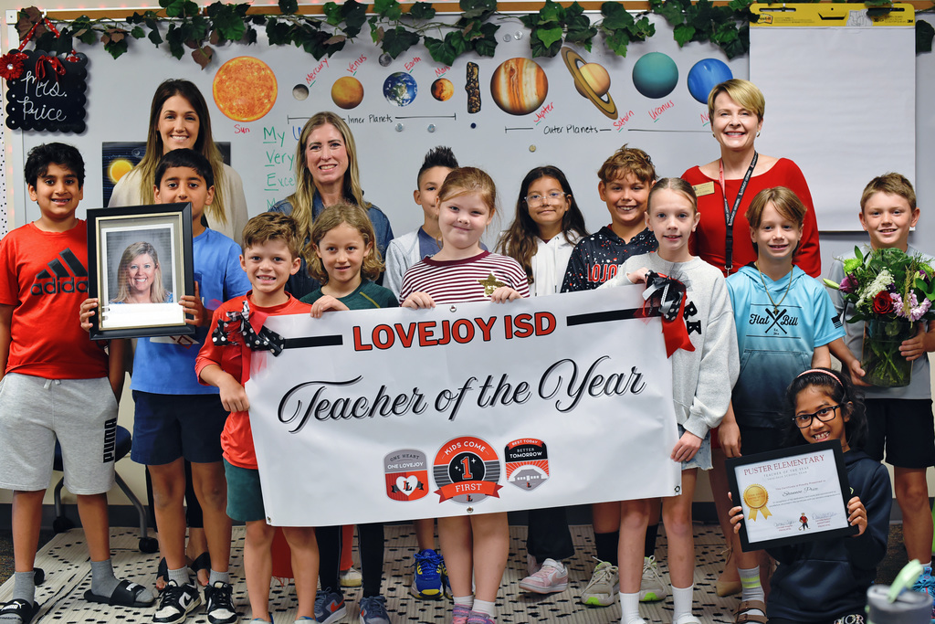 A group of children and two adults hold awards and a sign that reads "Teacher of the Year".