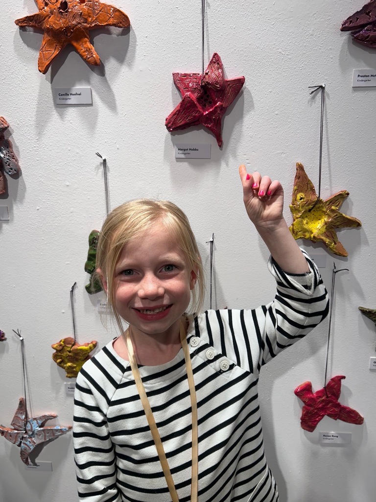 A child in a black and white striped shirt stands in front of a wall with colorful starfish decorations.
