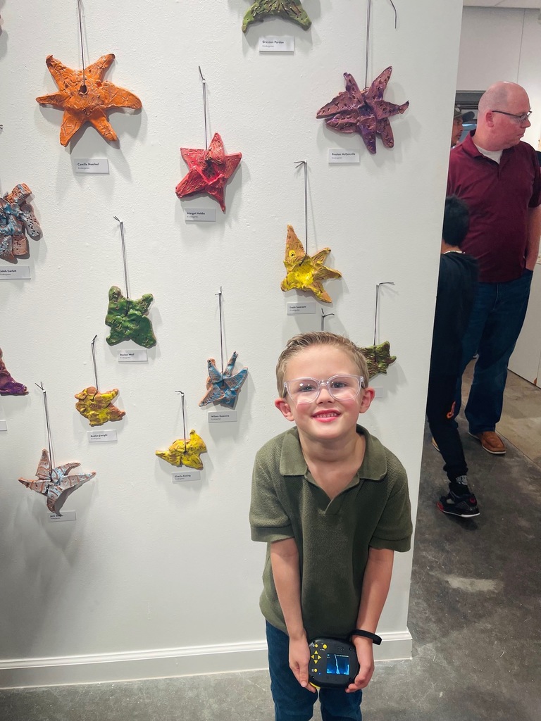 A young boy wearing glasses stands in front of a white wall displaying colorful starfish art.