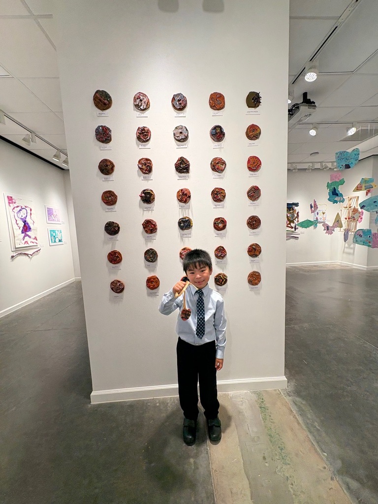 A child stands in front of a wall with many circular objects, possibly donuts, displayed in a museum setting.