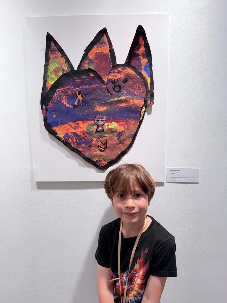 Child stands in front of a colorful painting of a cat-like figure on a white wall.