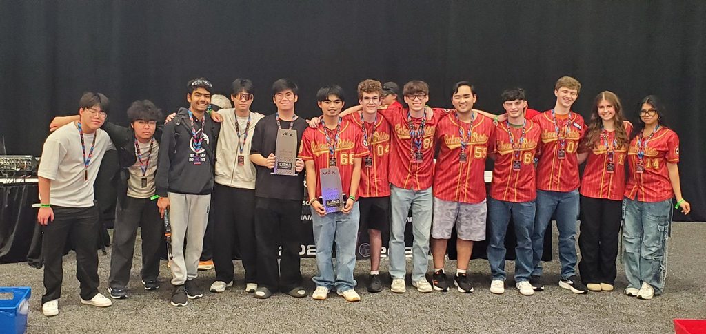 A group of young people in red shirts and jeans, standing on a stage with a black backdrop.