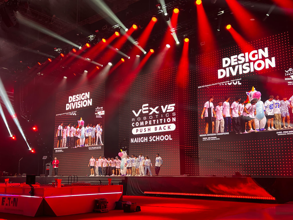 Bright stage with red lights and large screens showing "Design Division" and teams. Red lighting and spotlights.