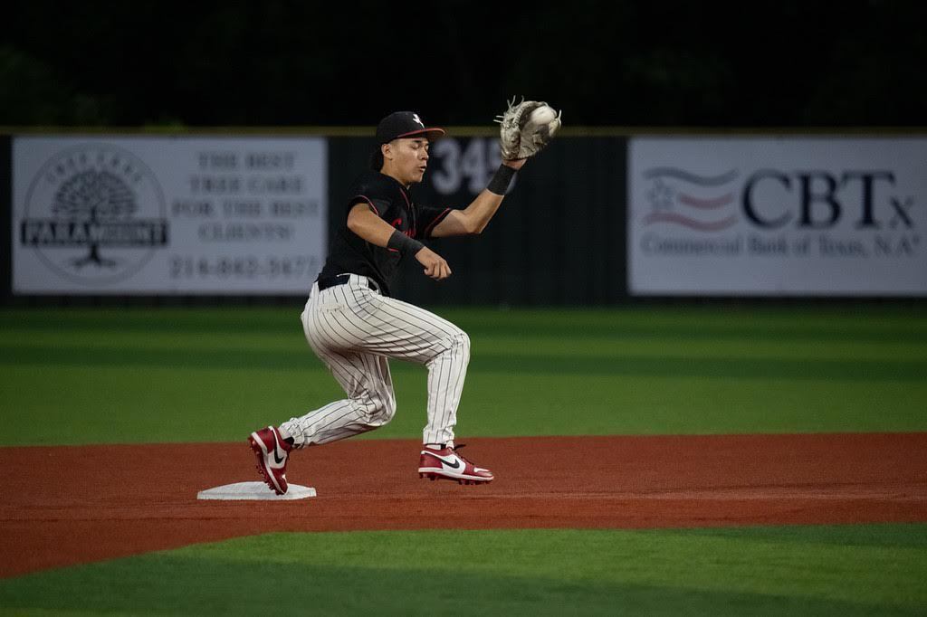 A baseball player in black and white uniform catches a ball in mid-air on a baseball field.