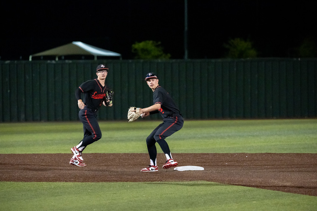 Two players in black uniforms on a baseball field at night. One player has a baseball glove.