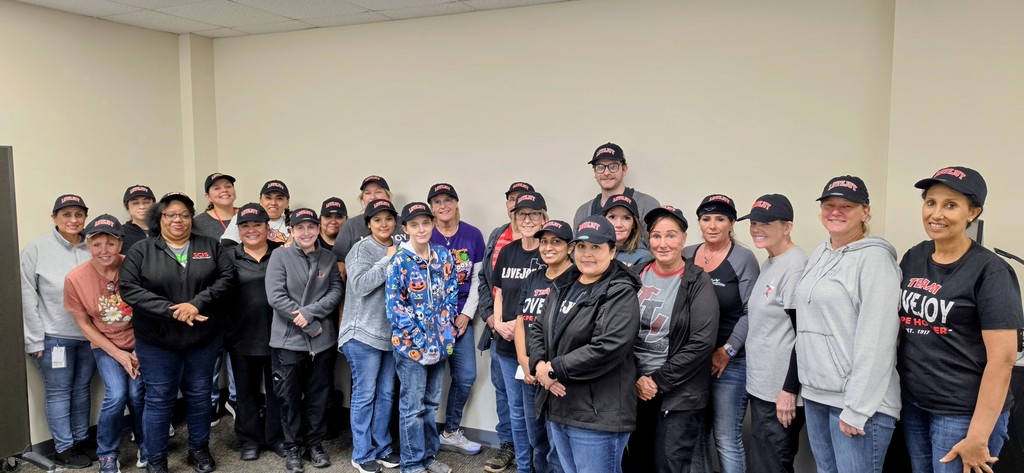 A group of people stands together in a room with white walls. They are wearing hats and jackets.