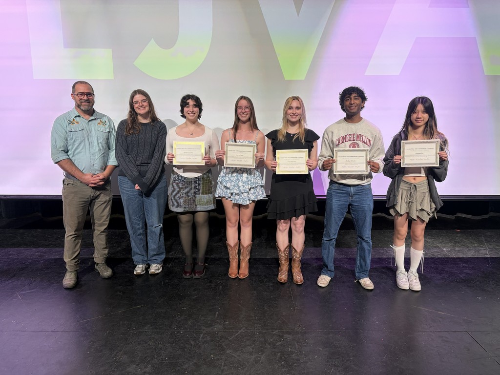 A group of individuals on a stage holding certificates. They stand in front of a multicolored screen.