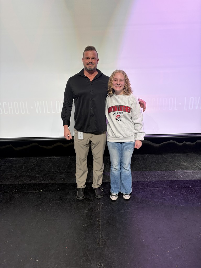 A man and a girl pose on a stage with a large screen in the background.