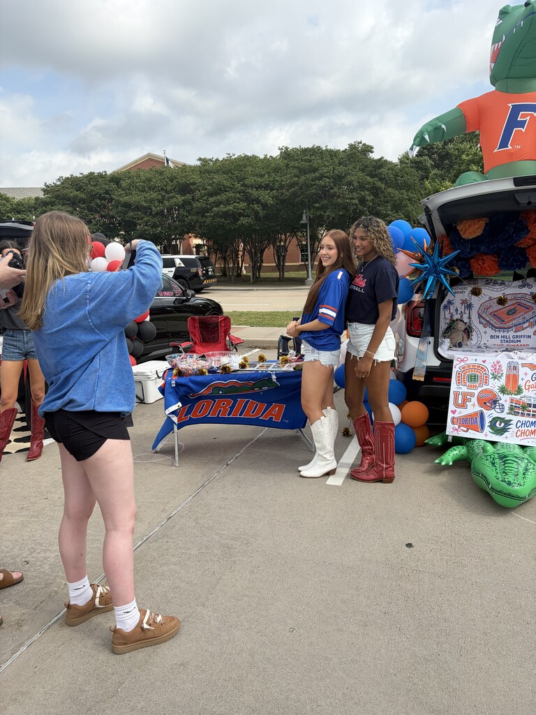 People in blue and white cheer for a Florida Gator float at an event on a cloudy day.