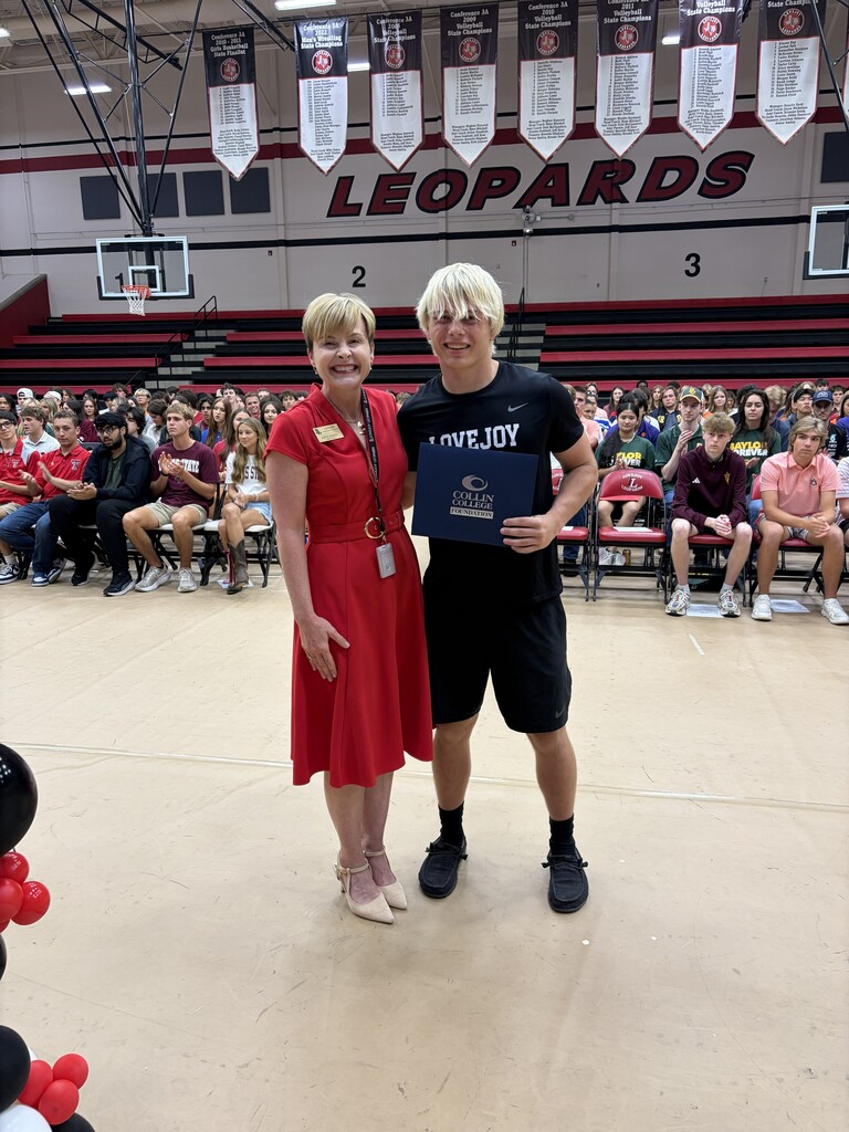 An adult woman and a man stand on a gym floor with a banner reading "Leopards" in the background.