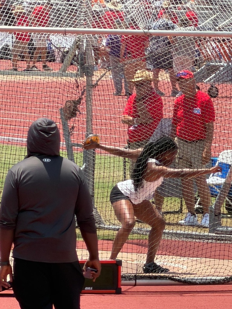 A woman throws a ball in a competition, wearing a white tank top. A man watches, wearing a gray shirt and black pants.