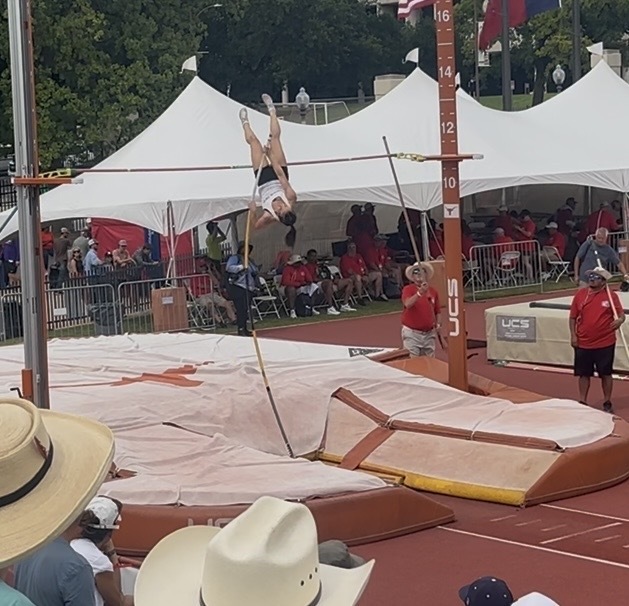 A person is performing a high jump on a track. Spectators are watching from white tents.