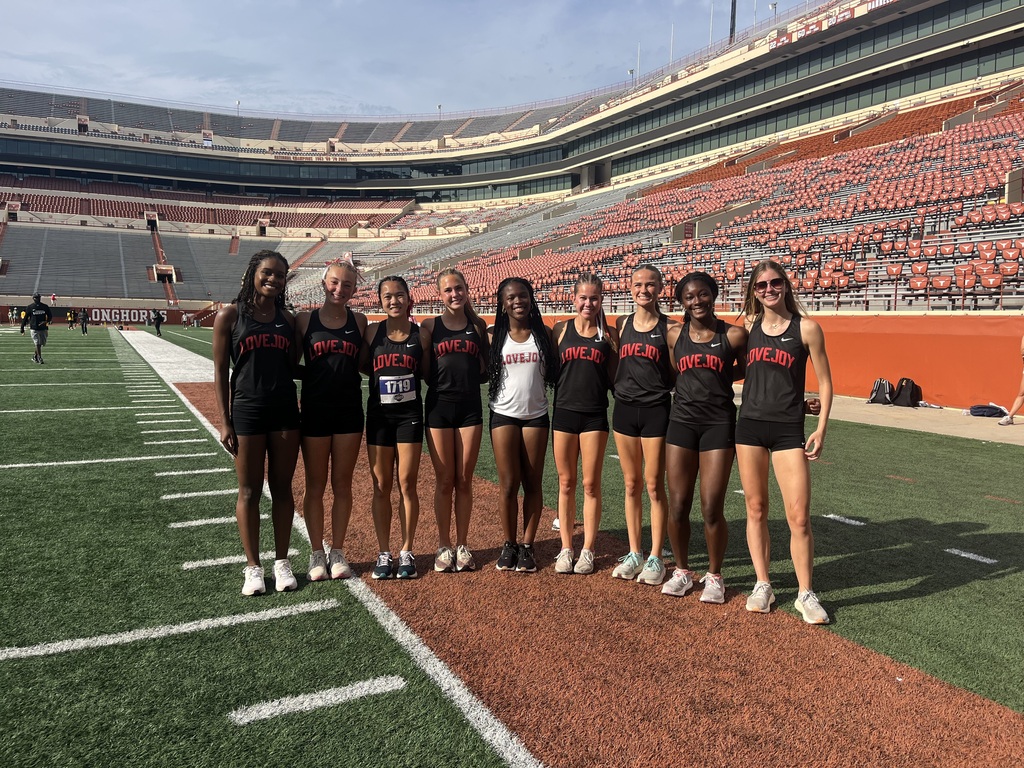 A group of women in black athletic uniforms and white sneakers on a football field.