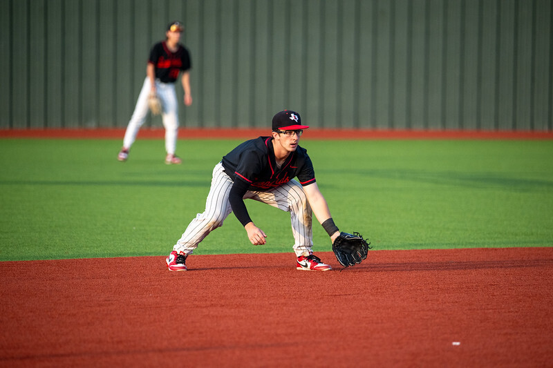 A baseball player in a black and white uniform bends to catch a ball on a field.