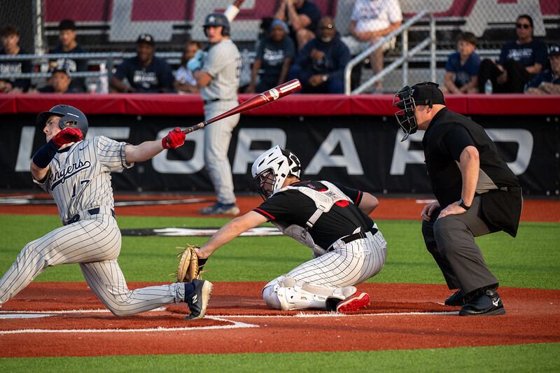 A baseball player swings at a pitch, another player slides in, and an umpire watches nearby.