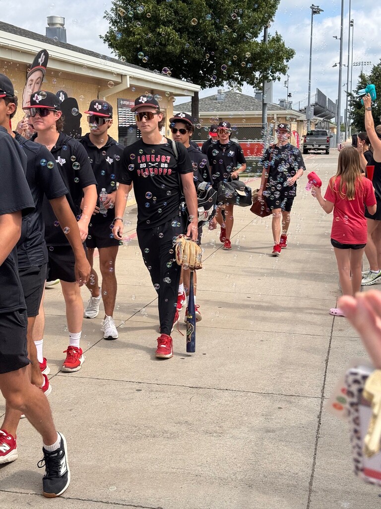 A group of baseball players with caps, sneakers, and some carrying gloves, walking on a sidewalk.