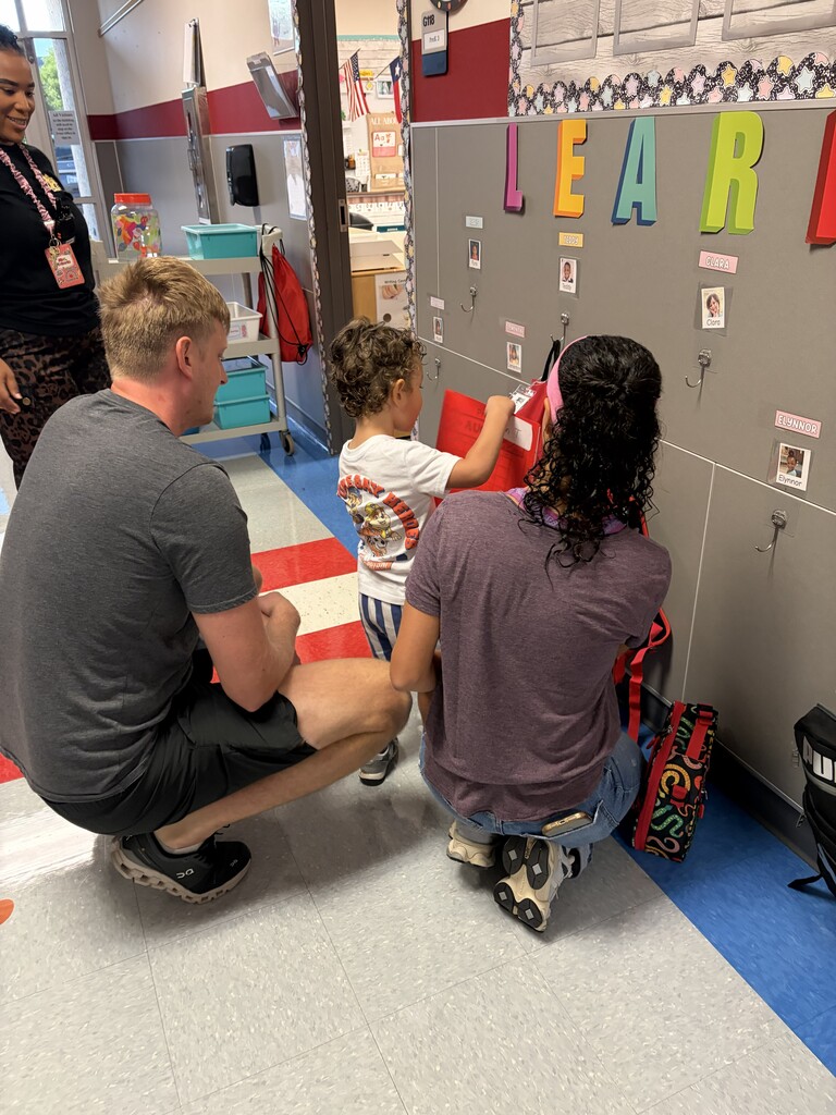 Adults kneeling in front of lockers. A child interacts with lockers. A woman stands behind them.