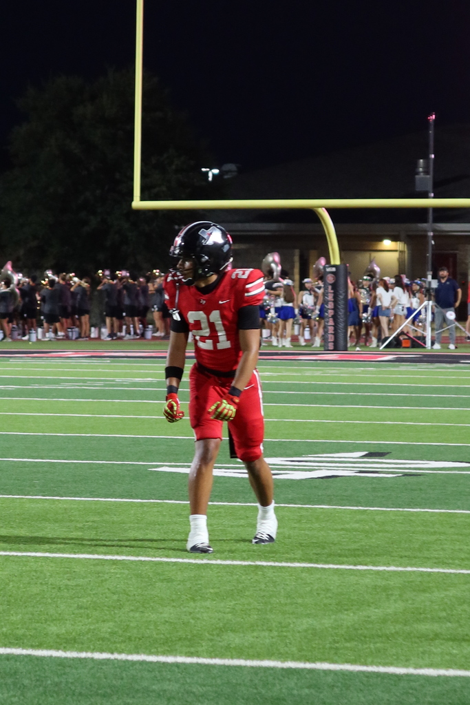 Player in red uniform, number 21, stands on the field at night, looking to the left.