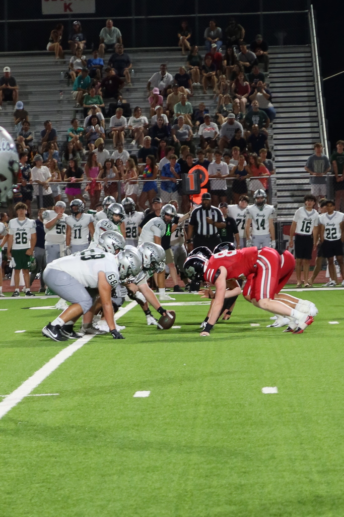 American football players in white and red uniforms playing on a field with a crowd of spectators in the background.