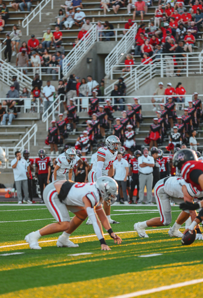 Football players in red and white uniforms on a field, with spectators in the background.