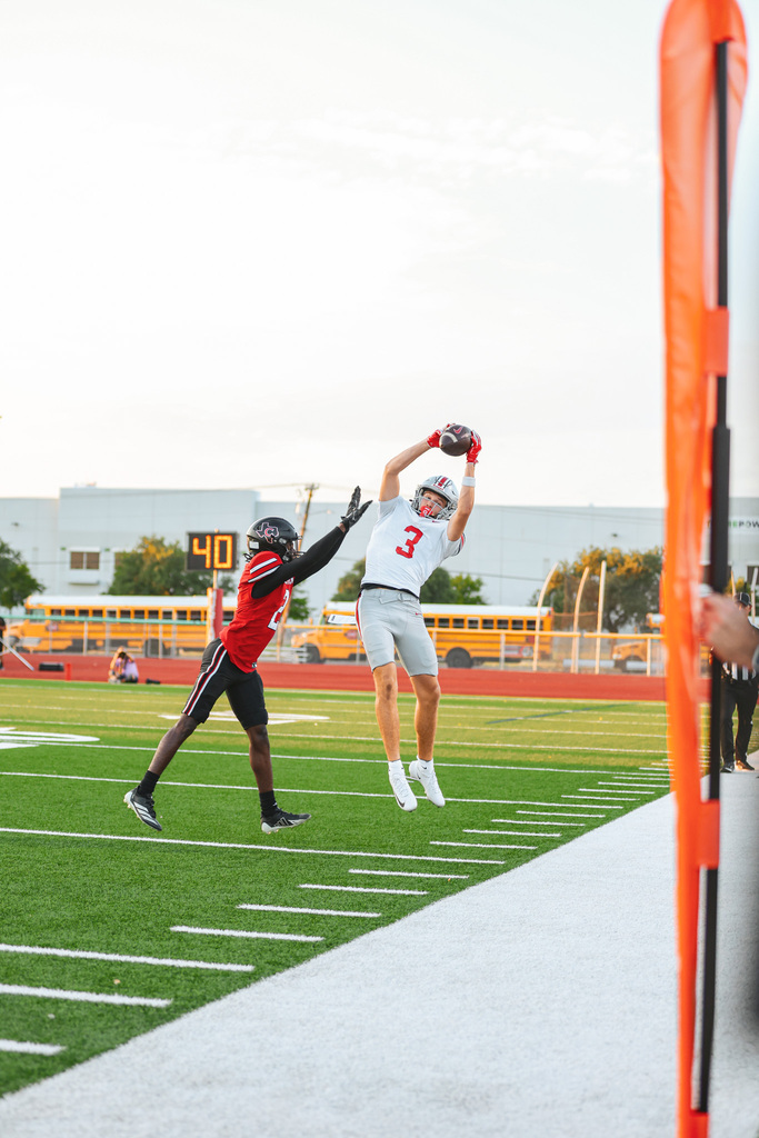 Two football players jumping in midair. One player is catching a ball. A yellow school bus is in the background.