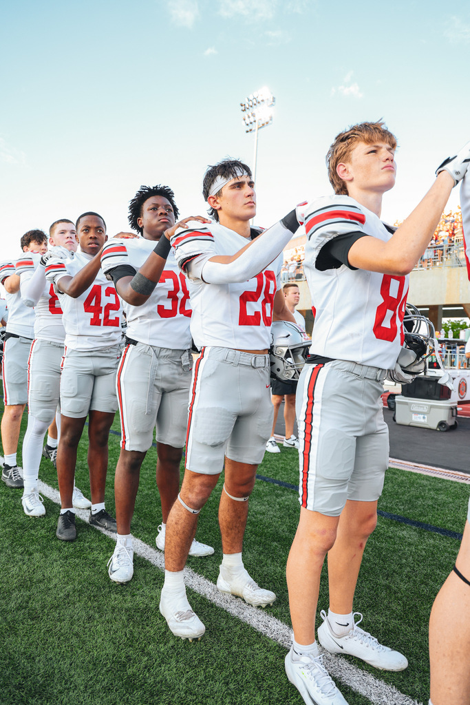 Football players in white uniforms and gloves stand on the field. Numbers on jerseys range from 8 to 42.