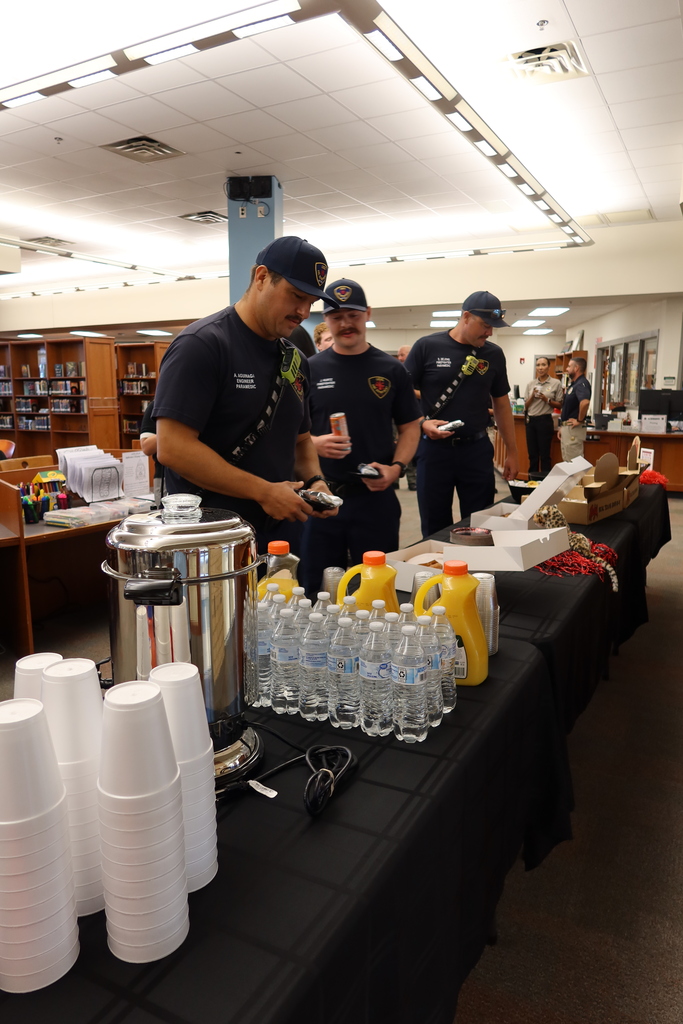 Four people in uniform prepare drinks at a long table with cups, bottles, and a coffee pot.