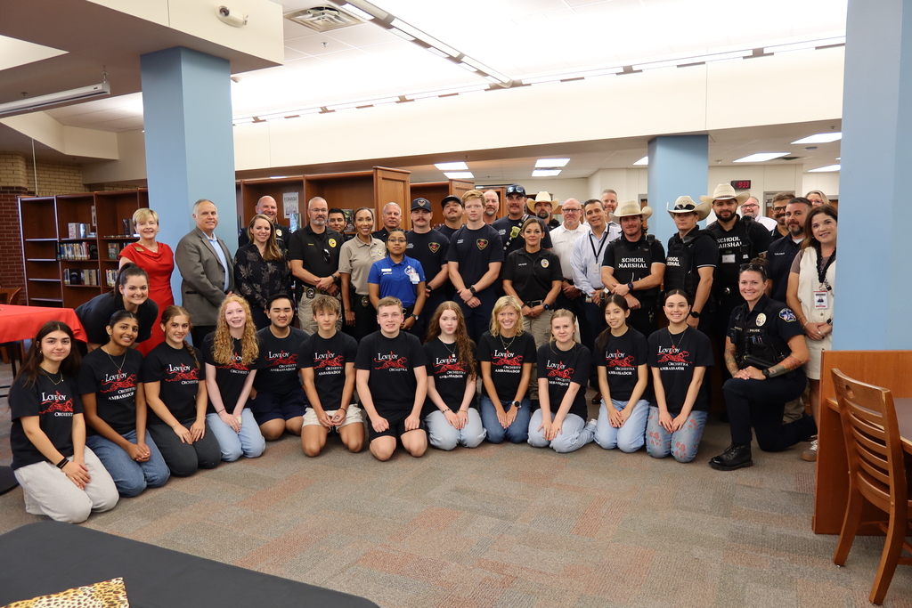 A group of uniformed officers and students in black t-shirts, some kneeling, some standing, in a library.