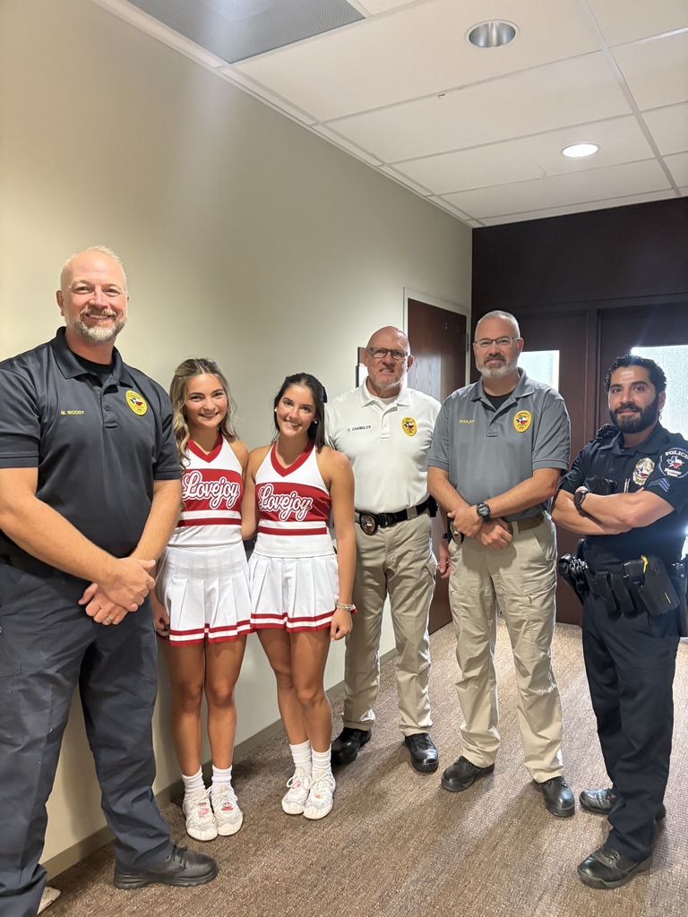 Six people stand in a room; two are cheerleaders in matching uniforms, and the others wear uniforms of different roles.