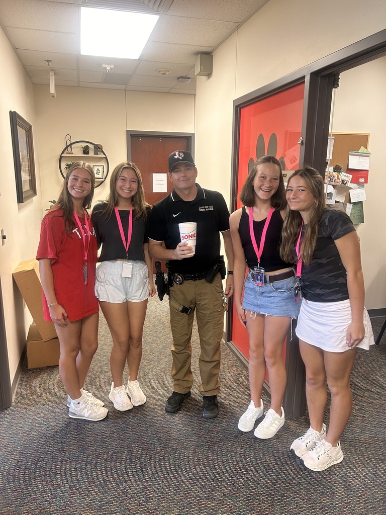 Five women and a man in a police uniform pose for a photo in a hallway.
