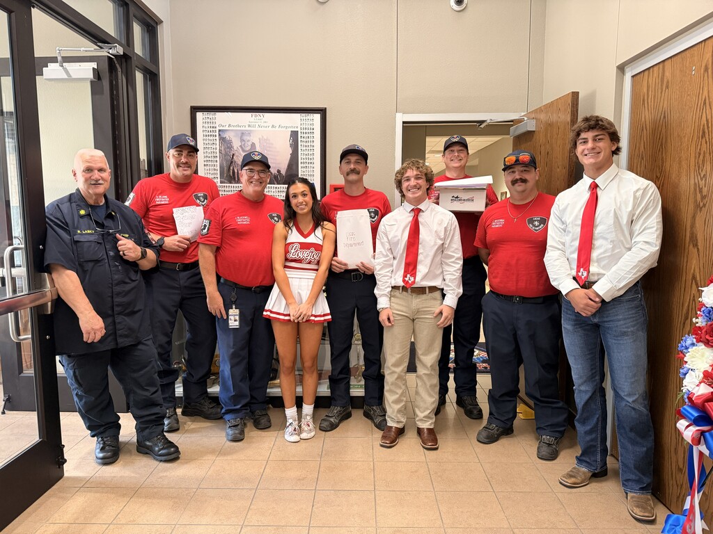 A group of people in red shirts and ties pose for a photo with a cheerleader in a hallway.