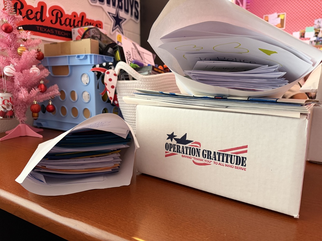 Desk with boxes of mail. One box has an open envelope on top. A small tree is next to a blue bin.
