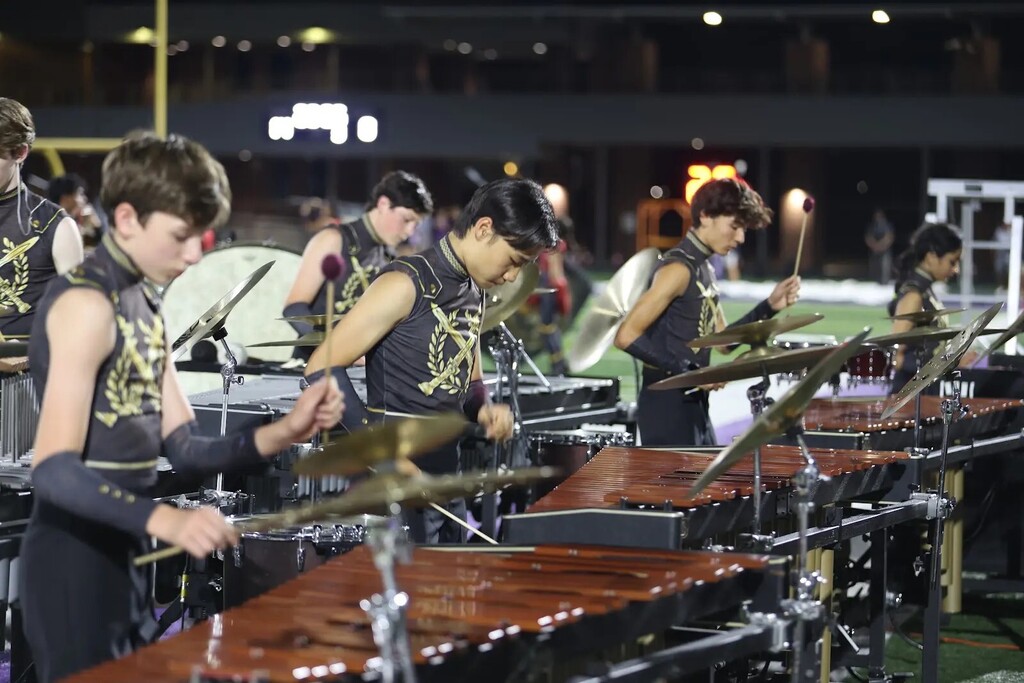 A group of students playing instruments on a stage at night. Instruments include xylophones and gongs.