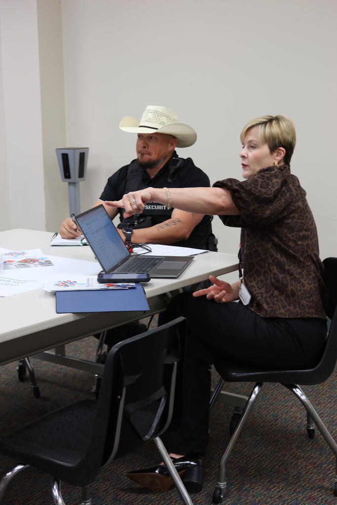 A woman and a man in a cowboy hat sit at a table, with the woman pointing at a laptop.