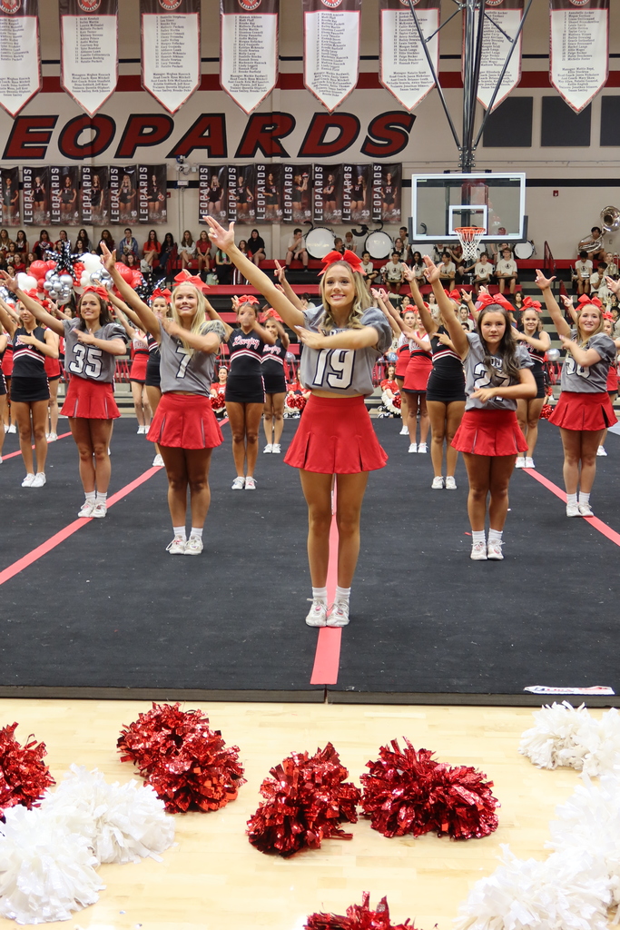 A group of cheerleaders in red and white outfits perform on a stage with red pompoms.