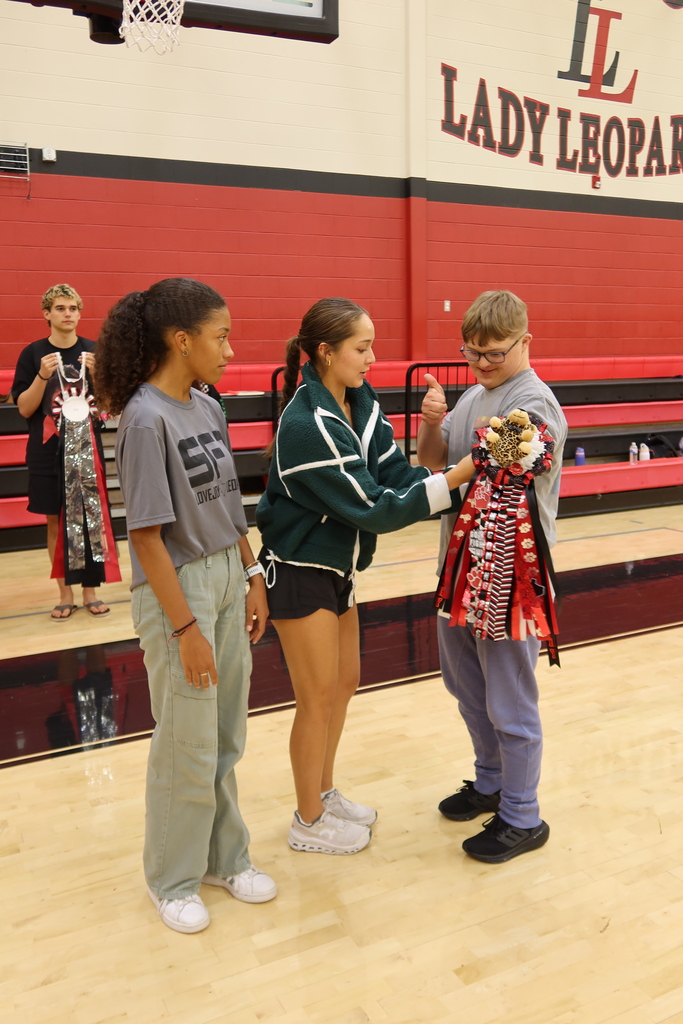 A group of students stands on a basketball court. One student holds a red and black pom pom.