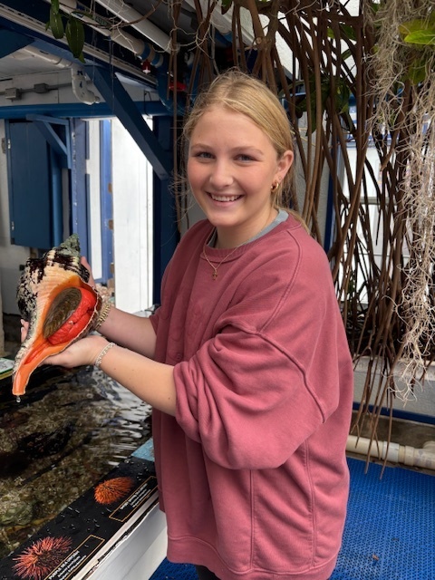 Student holding a large conch shell