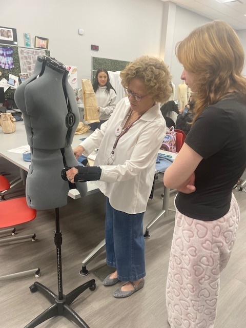 Teacher helping student adjust a manequin to the proper size