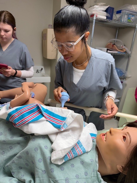 Allied health student simulating suctioning a newborn