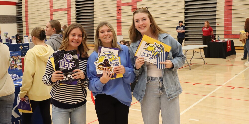 3 high school girls pose with college materials at the college fair
