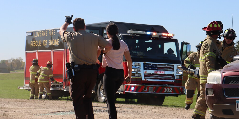 Sheriff Stratton walks student to ambulance as fire truck and fire workers work at the scene