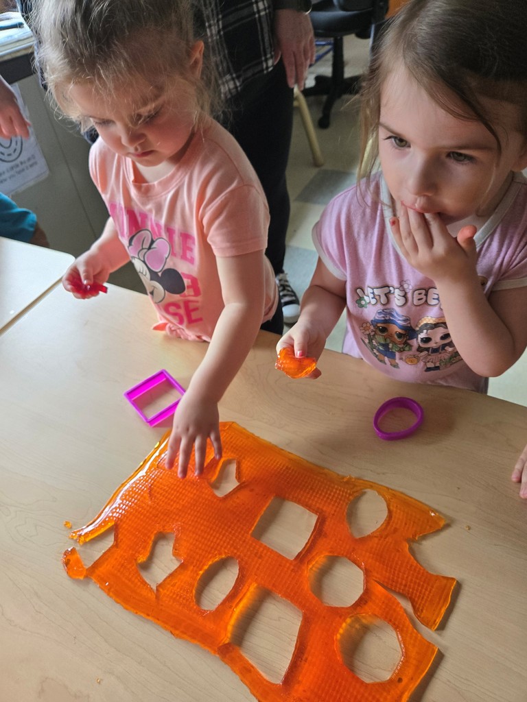 one student standing at table cutting shapes out of jello while another student eats jello