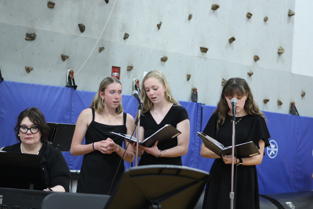 three girls singing together while woman plays piano
