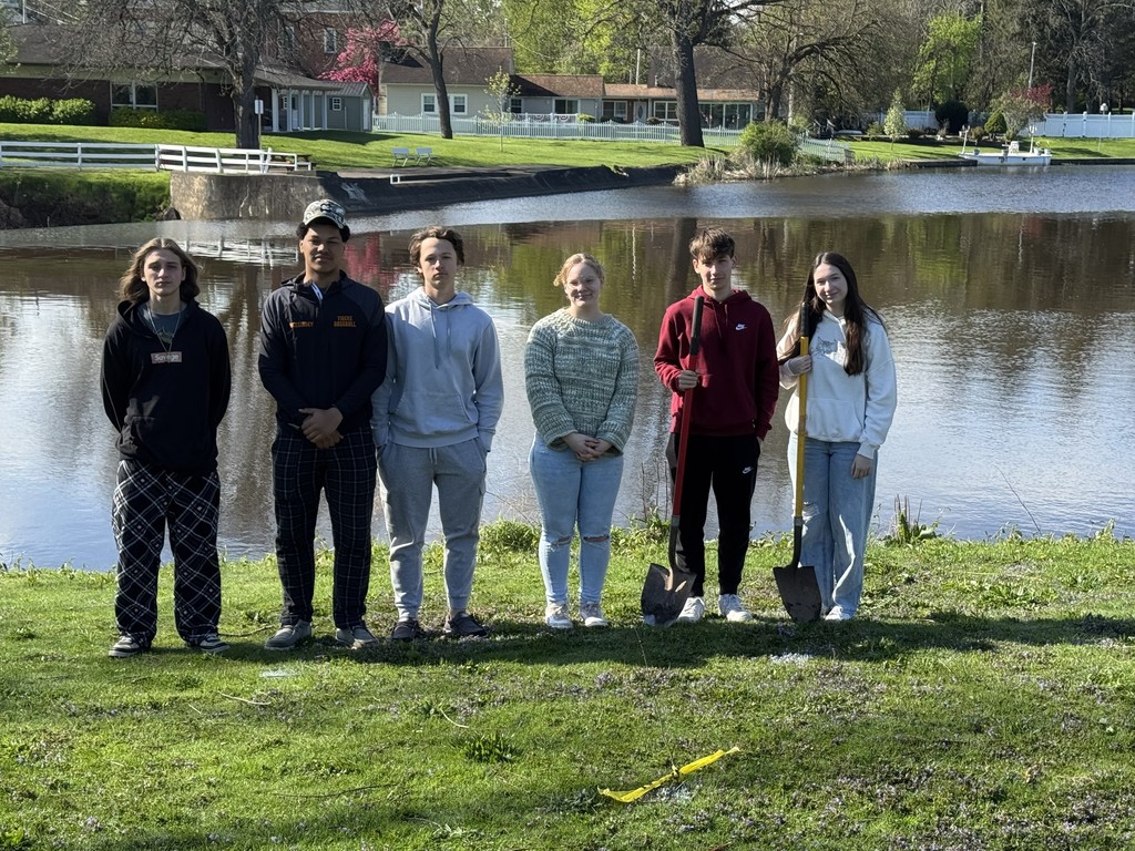 six students standing in front of river with shovels