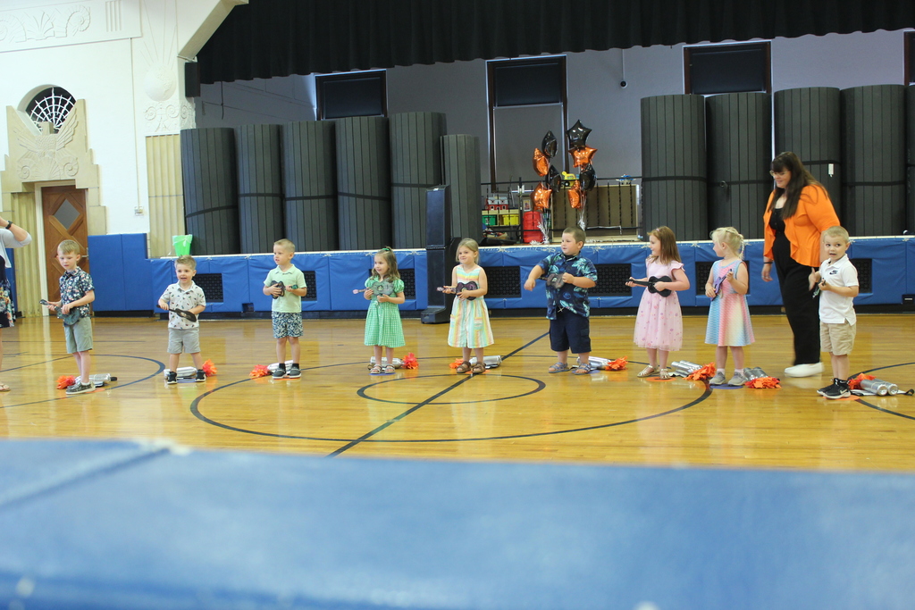 students standing in gym with teachers holding guitars singing a song