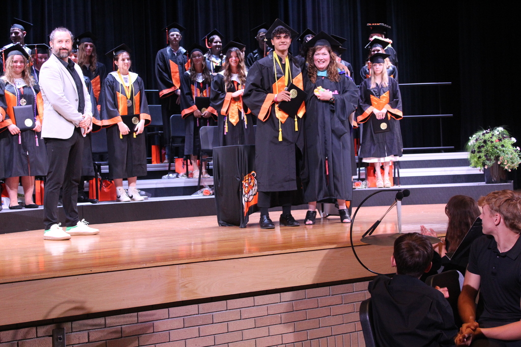 man standing on stage while graduating boy poses for a photo with woman