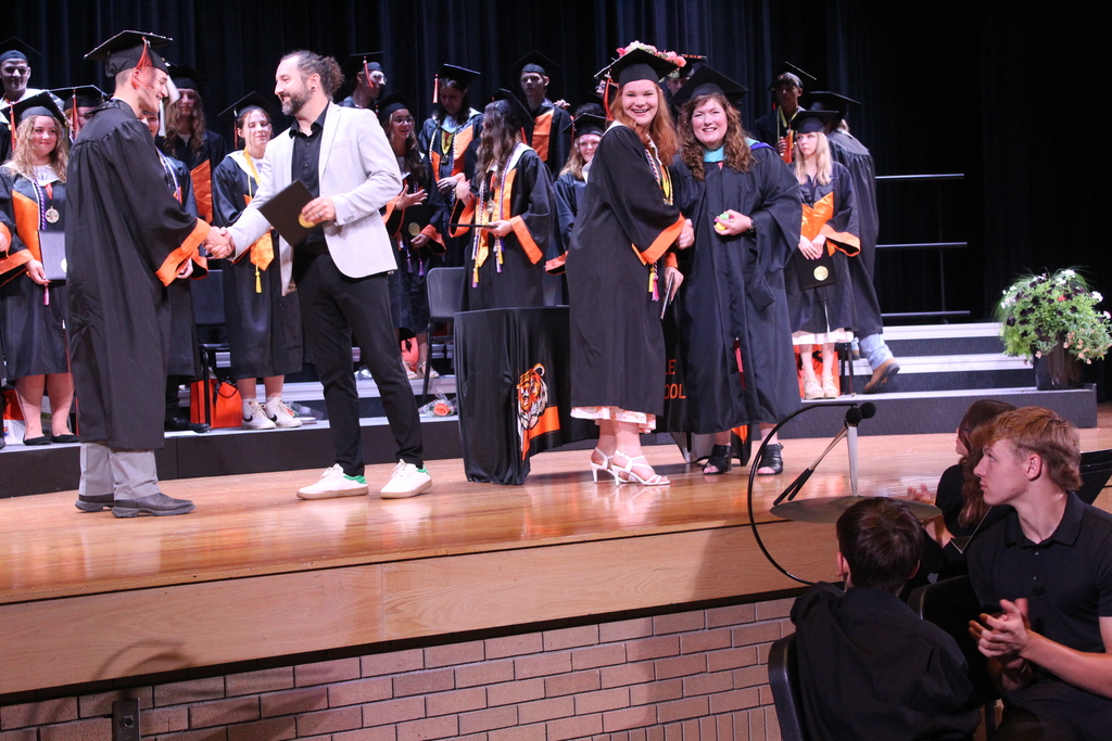 graduating boy shaking hand with man while graduating girl poses for a photo with woman